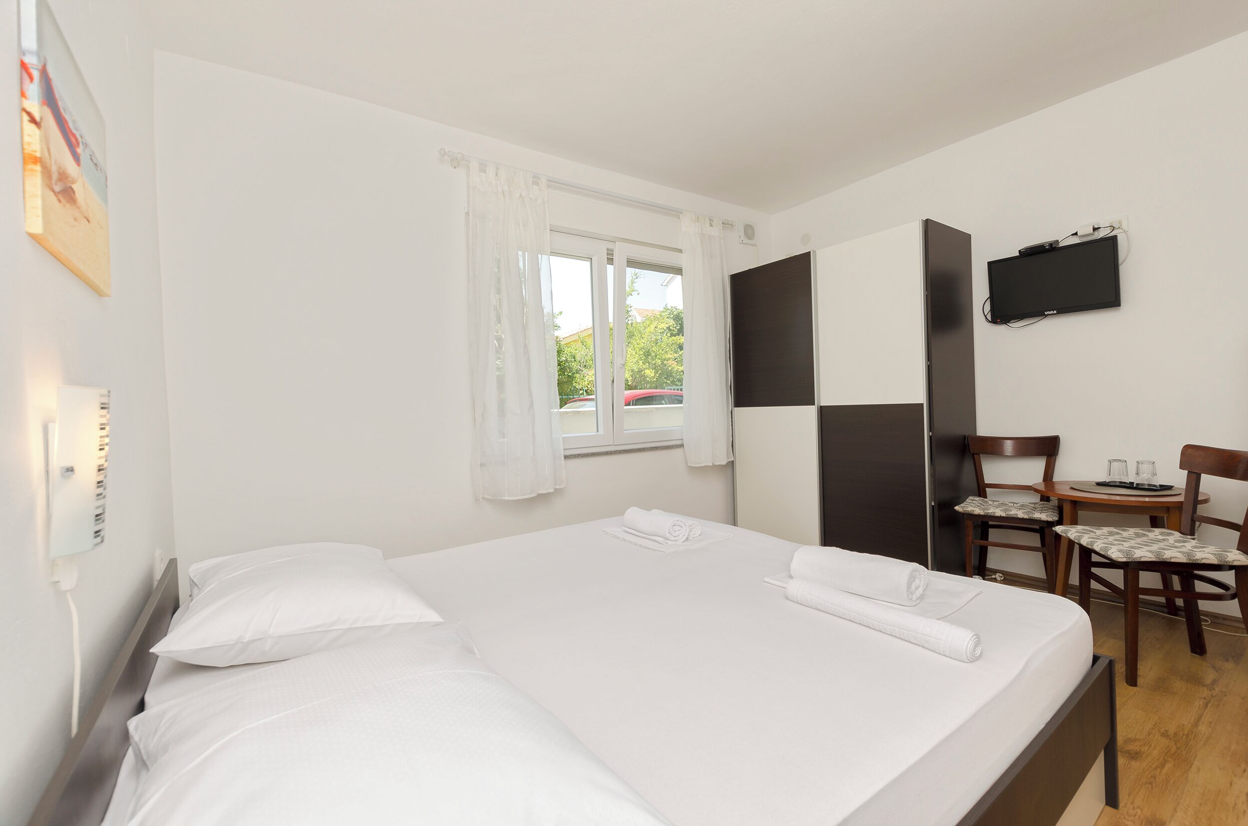 A hotel room with a bed, a desk, a chair, a flat-screen TV, and a window with curtains.
