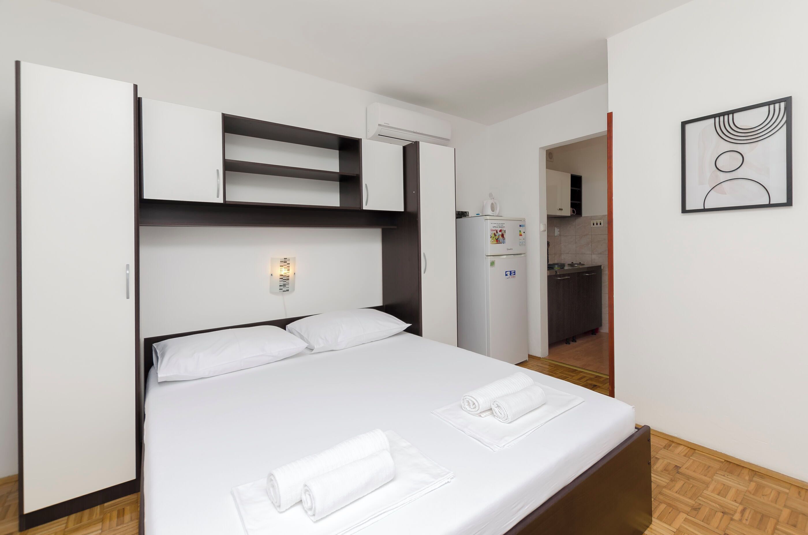 Een hotelkamer met een bed, een kledingkast, een kitchenette en een kunstwerk aan de muur.