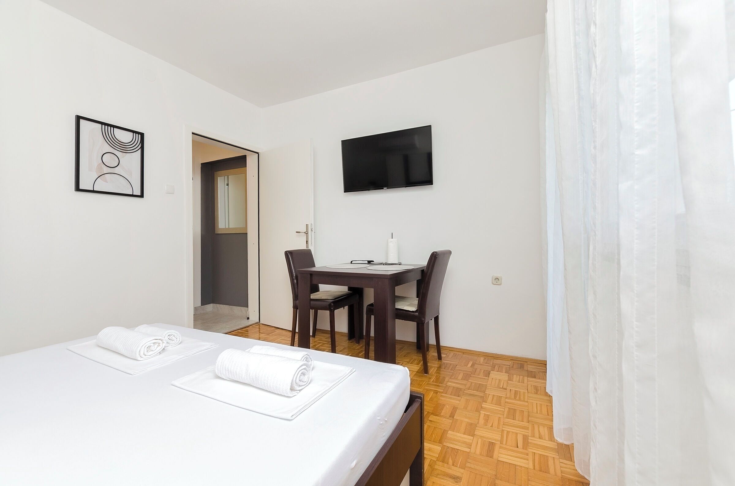 A hotel room with a bed, a desk, a chair, a TV, and a door.