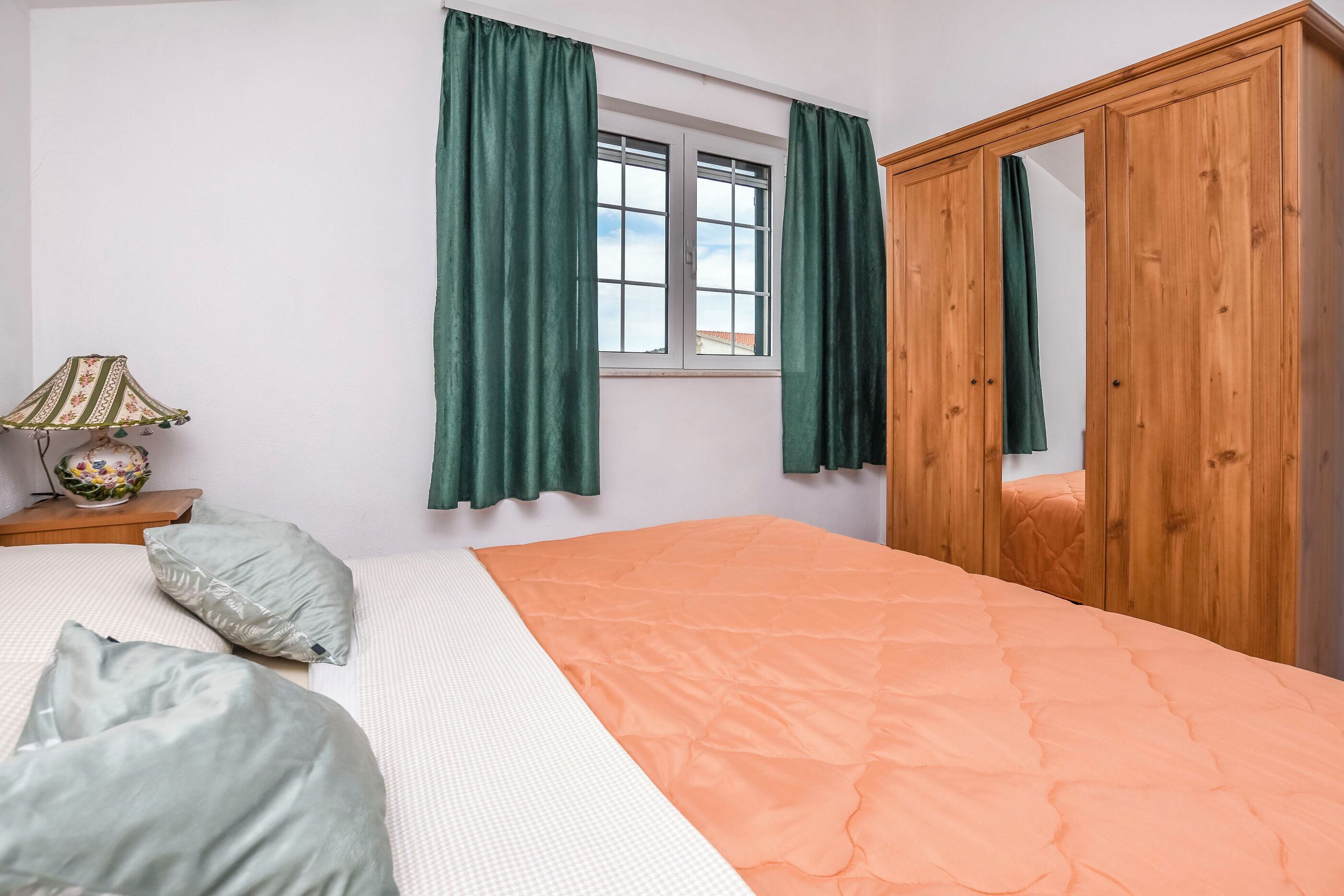 Een slaapkamer met een bed, groene gordijnen, een houten garderobe en een raam.