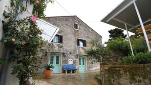 Un callejón estrecho con un edificio que tiene dos puertas verdes, un banco azul y plantas en macetas.
