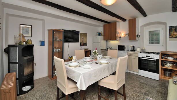 Un comedor con una mesa dispuesta para cuatro, armarios de madera, horno empotrado y un televisor en la pared.
