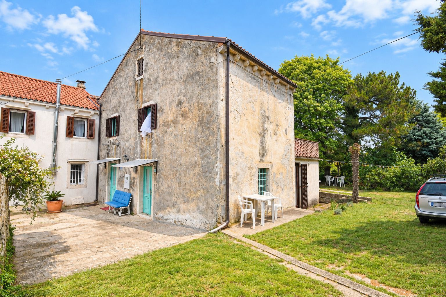 A two-story building with a stone facade, a small patio with a table and chairs, and a car parked outside.