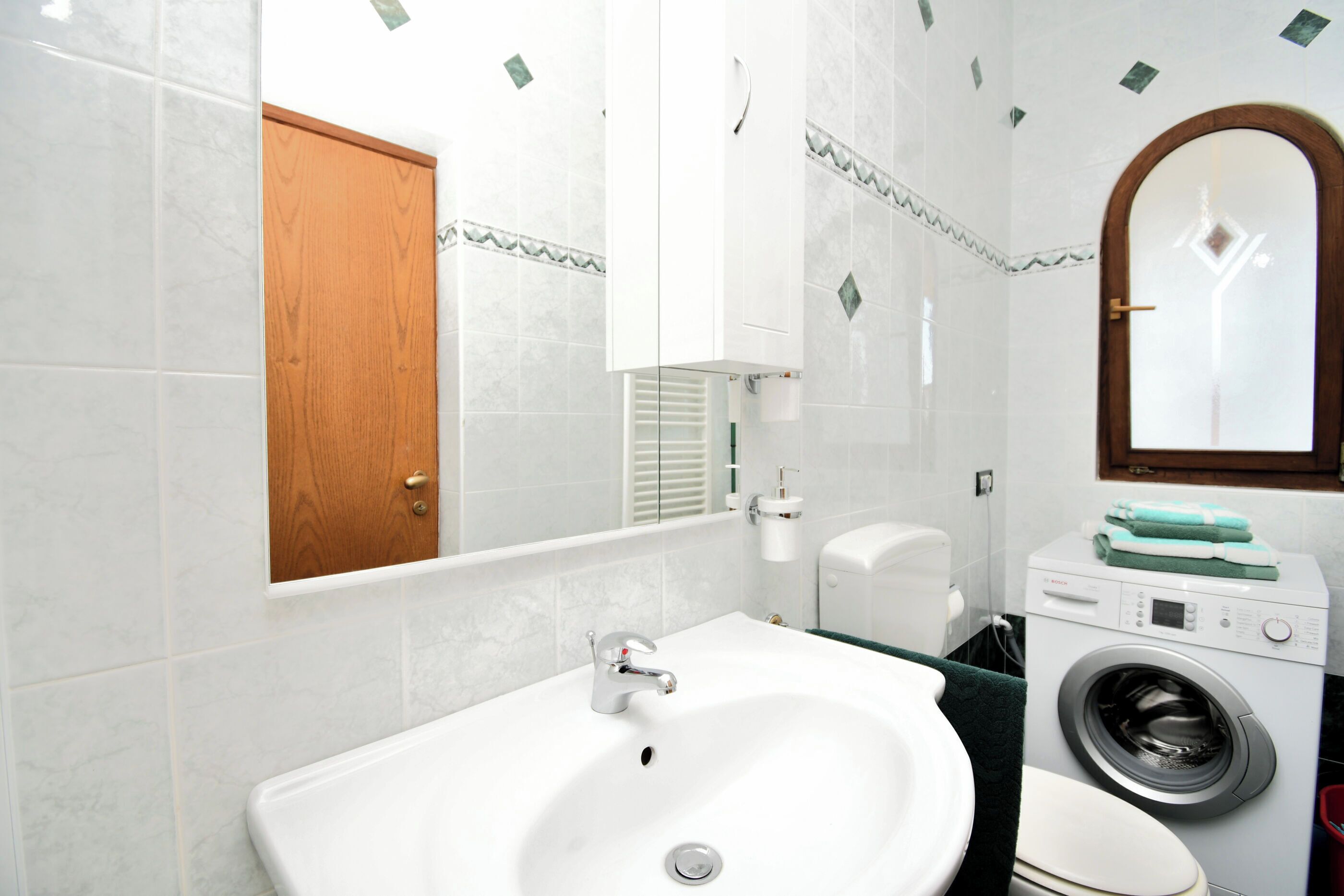 A bathroom with a white sink, a wooden door, a washing machine, and a toilet.