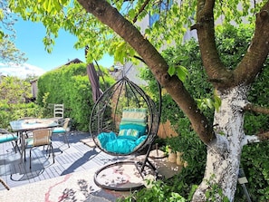 Un fauteuil suspendu avec des coussins, une table avec des chaises et une terrasse en bois.