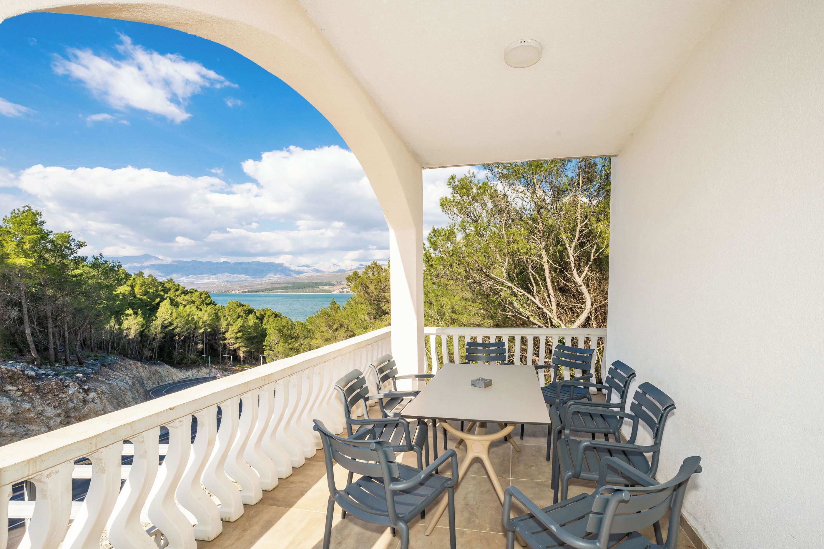A covered outdoor seating area with a table and chairs, overlooking a scenic landscape with trees and a body of water.