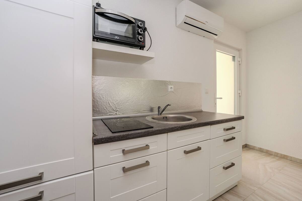 Een moderne keuken met witte kasten, een granieten werkblad, een ingebouwde magnetron en een airconditioner.