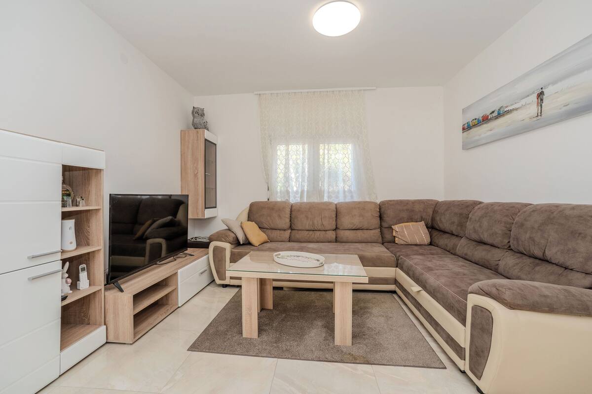 Een moderne woonkamer met een hoekbank, een glazen salontafel, een flatscreen televisie en inbouwplanken.