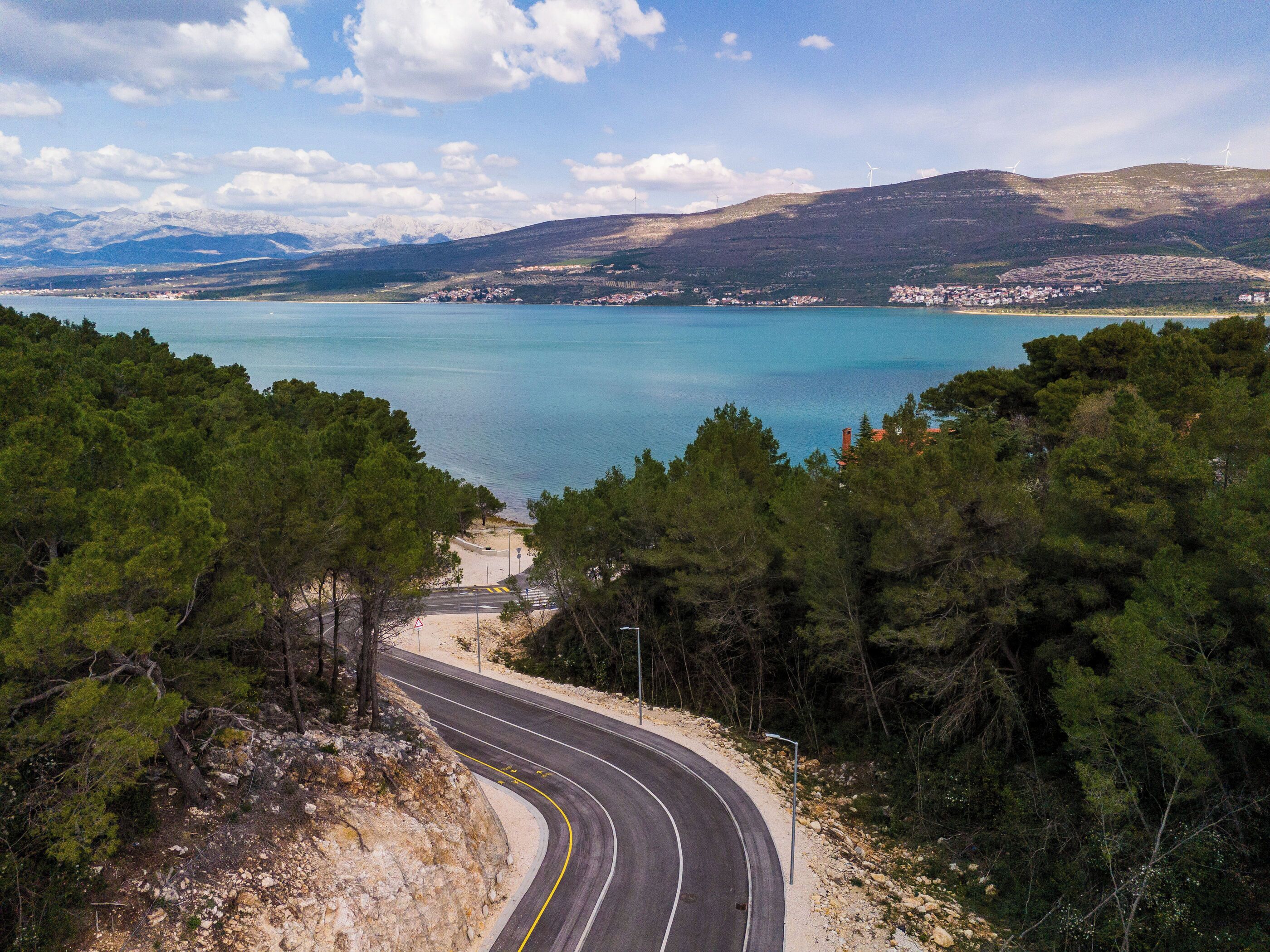 A winding road leading to a coastal area with a view of the sea and distant mountains.
