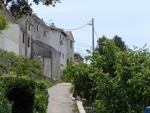 A narrow street with a building on the left, surrounded by greenery. - Apartments Rose (Mali Losinj)
