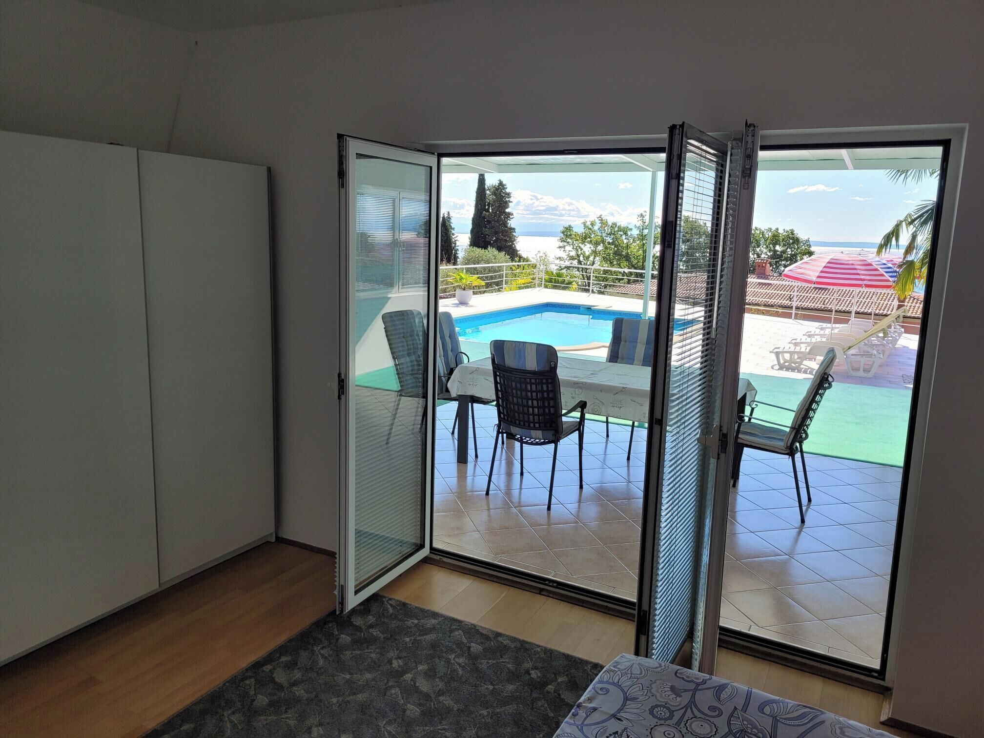 A room with a sliding glass door leading to an outdoor pool area with chairs and a table.