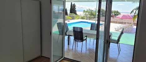 A room with a sliding glass door leading to an outdoor pool area with chairs and a table.