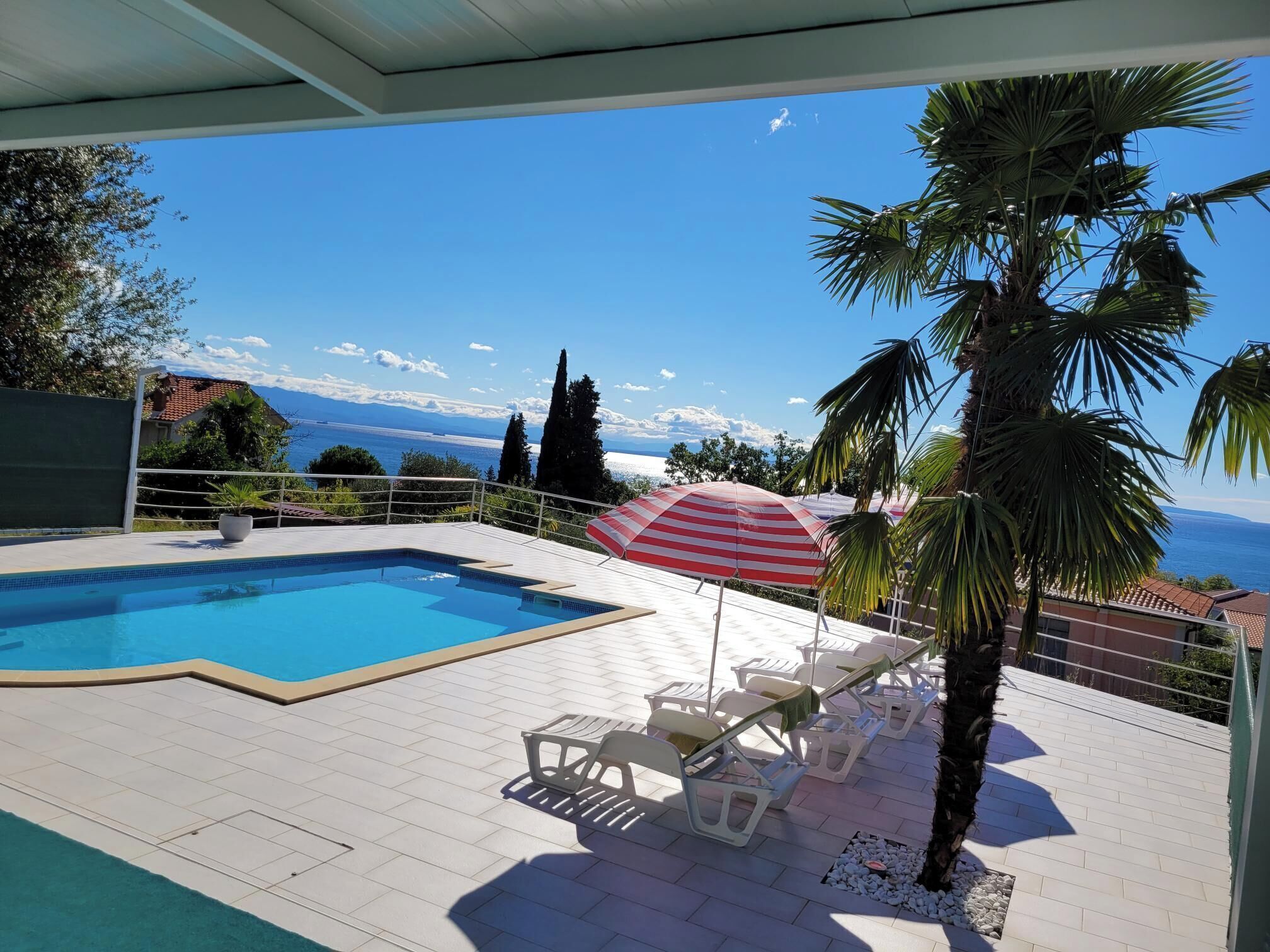 A swimming pool with lounge chairs and an umbrella, overlooking a scenic view of the sea and mountains.