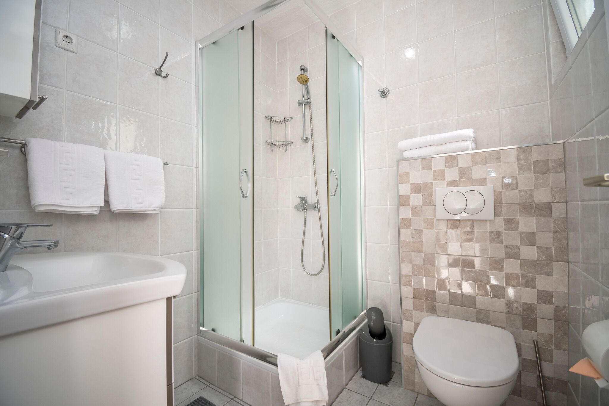 A modern bathroom with a glass-enclosed shower, a white sink, and a toilet.