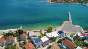 An aerial view of a coastal town with clear blue waters, a pier, and residential buildings. - Apartment Filipovic (Bilice)