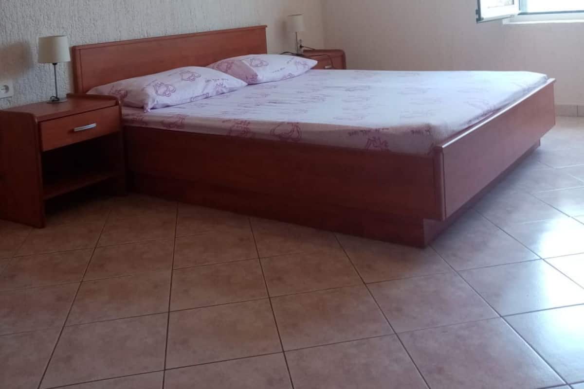 A bedroom with a single bed, a nightstand, a lamp, an air conditioning unit, and a window.