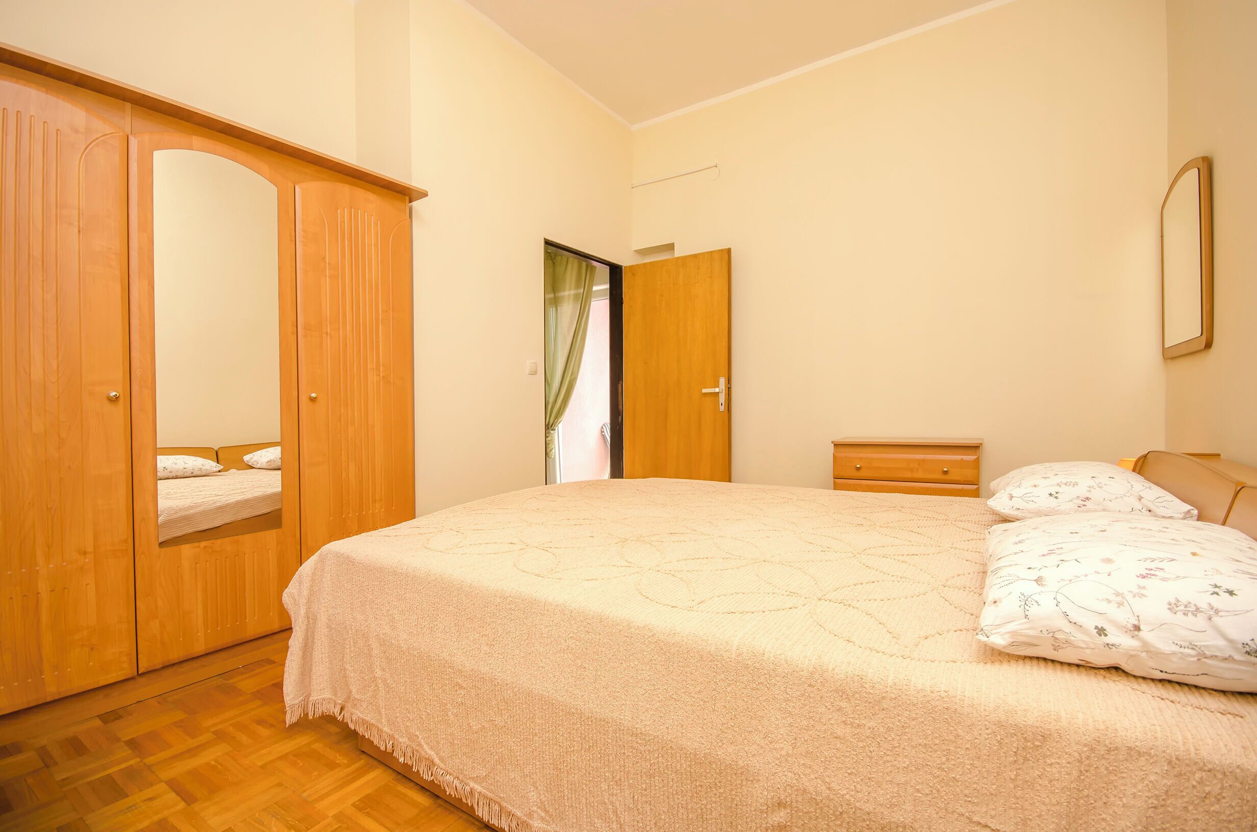 Ein Schlafzimmer mit einem Bett, einem Holzschrank, einem Nachttisch und einem Spiegel an der Wand.