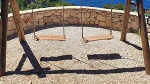 A wooden swing set with a sign that reads "Visit TRIBUNJ" against a backdrop of a clear blue sea and a rocky landscape. - Apartments Peaceful Port (Tribunj)