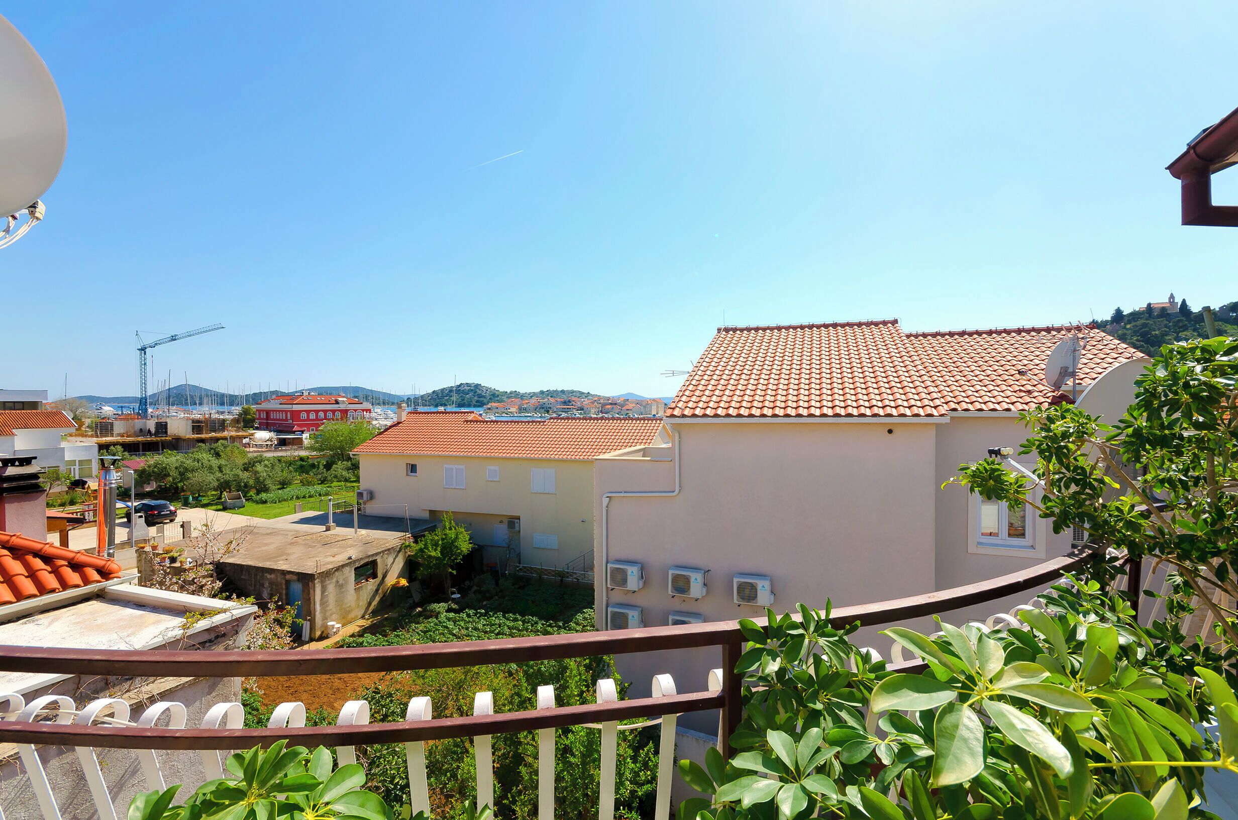 A residential area with terracotta-tiled roofs, satellite dishes, and a clear blue sky.