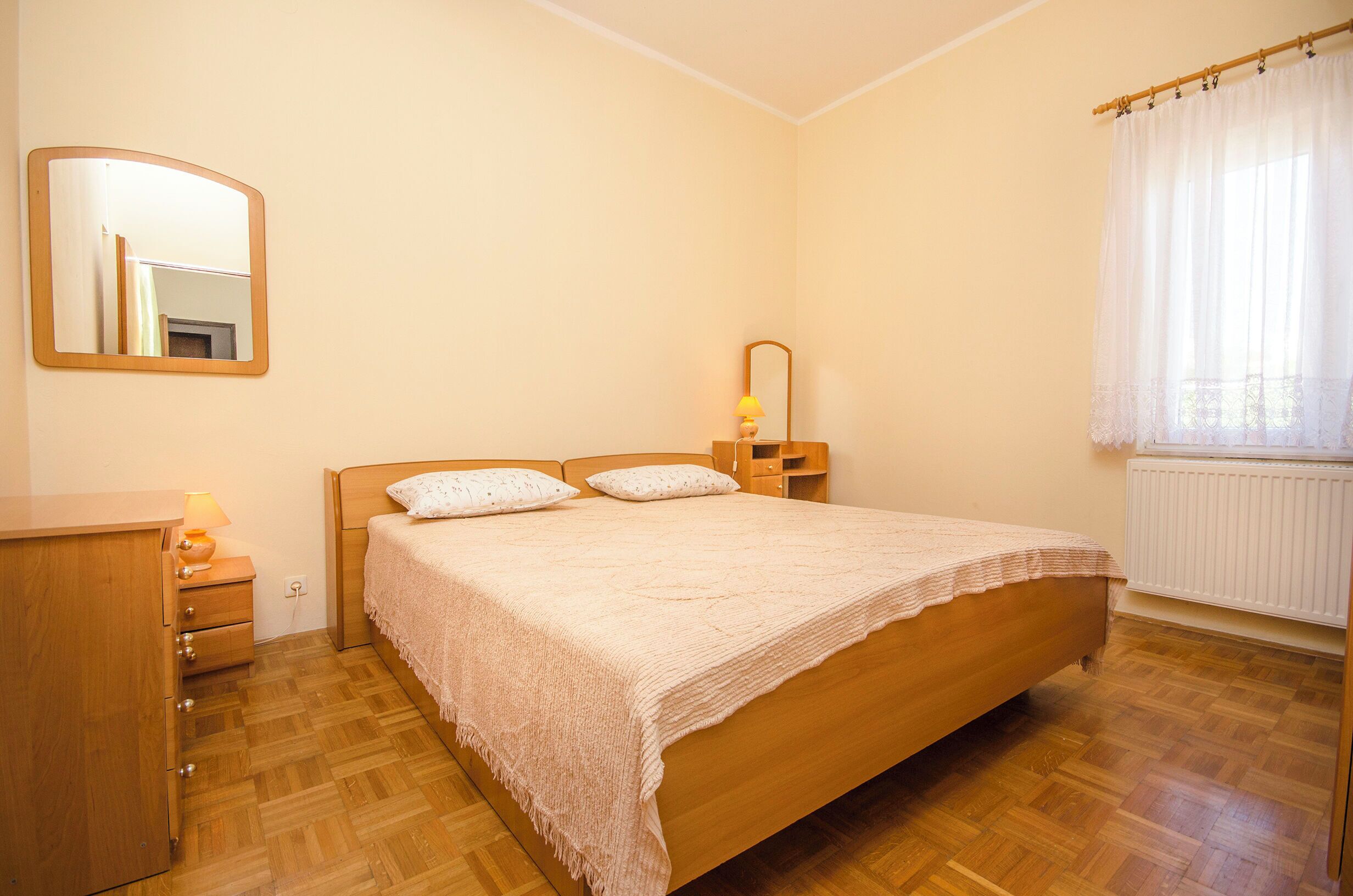 A bedroom with a wooden bed, a nightstand, a mirror, and a window with curtains.