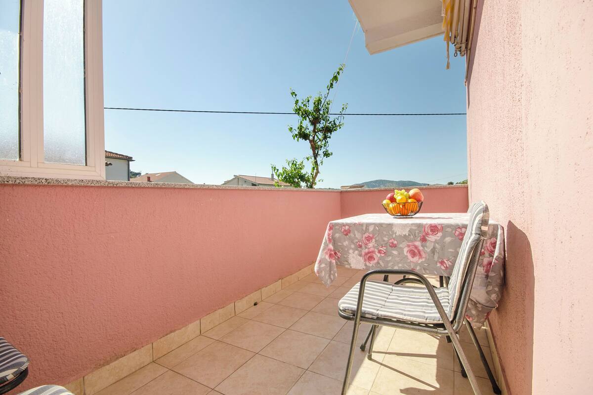 A balcony with a table and chairs, a small tree, and a view of distant buildings.