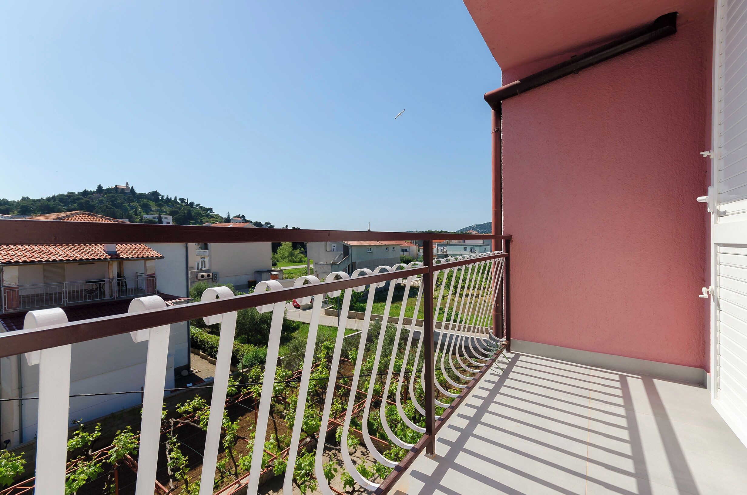 A balcony with a metal railing overlooking a garden and buildings.