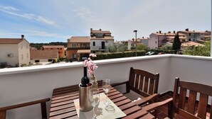 A balcony with a table set for two, featuring a wine bottle, glasses, and a vase with flowers. - Apartment Honey Bee (Pula)