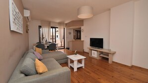 A modern living room with a grey sofa, a white coffee table, and a flat-screen TV on a wooden stand. - Apartment Honey Bee (Pula)
