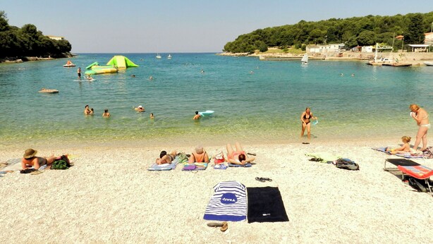 A beach with clear water, people swimming and sunbathing, and a few boats in the distance. - Apartment Honey Bee (Pula)