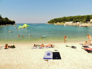 A beach with clear water, people swimming and sunbathing, and a few boats in the distance. - Apartment Honey Bee (Pula)