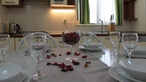 A dining table set with wine glasses and plates, a bowl of rose petals, and a kitchen in the background. - Apartment Marijela (Vela Luka)