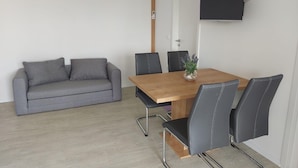 Ein modernes Wohnzimmer mit grauem Sofa, einem Holzesstisch mit sechs Stühlen und einem flachbildfernseher an der Wand.