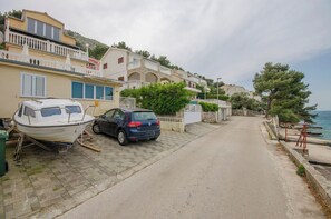 A coastal street with parked cars and a boat, houses with balconies, and a view of the sea. - Apartment Seafront (Sibenik)