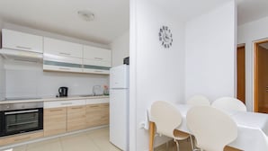 Una cocina moderna con armarios blancos, horno empotrado y refrigerador. Hay un comedor con mesa y sillas.