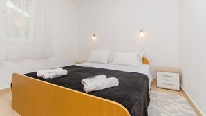 Un dormitorio limpio y minimalista con una cama de madera, ropa de cama blanca y una mesita de noche pequeña.