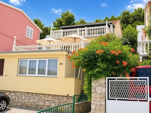 A yellow building with a balcony, a stone wall, and a red car parked in front. - Apartment Seafront (Sibenik)