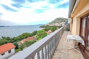 Un balcone con tavolo e sedie, vista su una cittadina costiera e il mare.