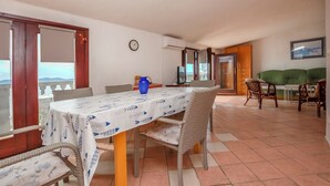 A dining area with a table covered by a patterned tablecloth, wicker chairs, and a blue vase. - Apartments Marinero (Pakostane)