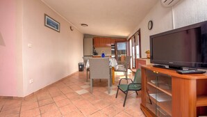 A living room with a TV, a dining area with chairs, a kitchen in the background, and a tiled floor. - Apartments Marinero (Pakostane)