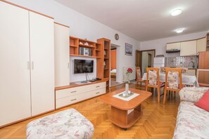 Una sala de estar con sofá, reposapiés, mesa de centro de madera, televisor y estanterías empotradas.
