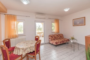 Una habitación con una mesa de comedor, sillas, un sofá, una mesita con un jarrón y un cuadro en la pared.