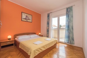 Une chambre à coucher avec un lit, des tables de chevet, un tableau et une grande fenêtre avec des rideaux.