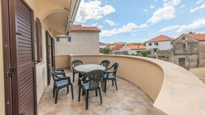 A balcony with a round table and chairs, a curved wall, and a view of neighboring buildings. - Apartments Murter Jurjako (Murter-Kornati)