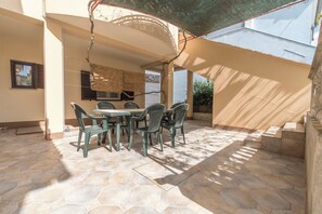 Un patio al aire libre con suelo de piedra hexagonal, una mesa con sillas y una pérgola que ofrece sombra.