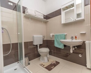 Une salle de bain avec une douche à parois de verre, des toilettes, un lavabo avec un miroir au-dessus et un porte-serviettes avec des serviettes pliées.