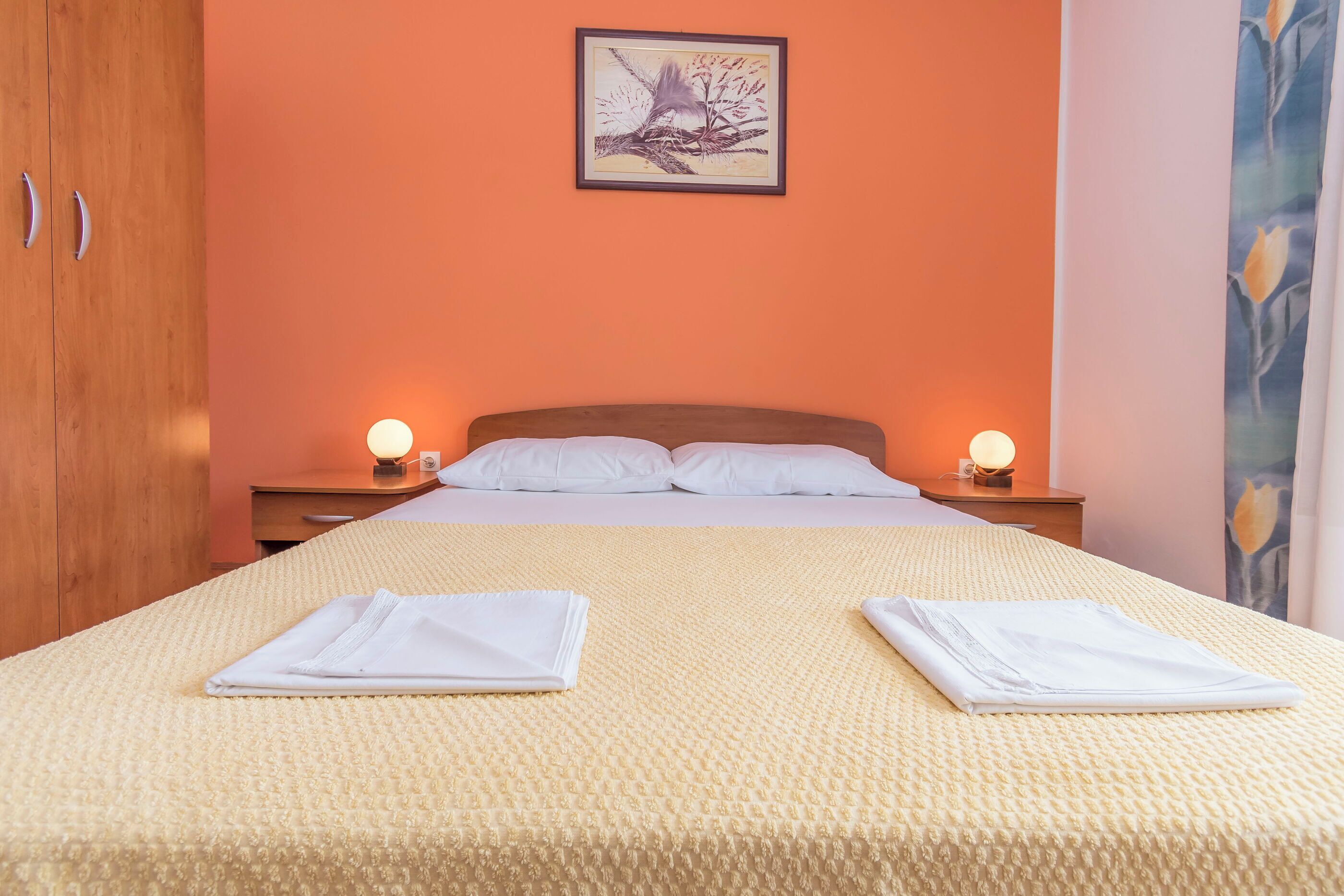 A neatly made bed with white linens, two bedside lamps, and a framed artwork on the wall.