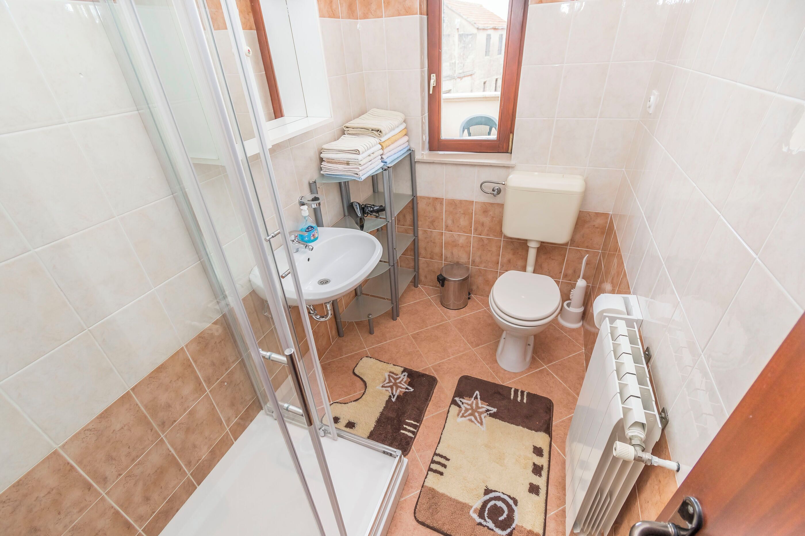 Un bagno compatto con cabina doccia in vetro, lavandino, water e termosifone.