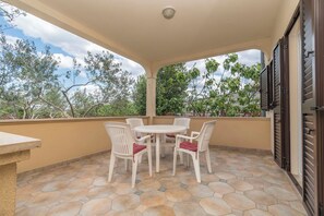 A covered patio with a round table and chairs, beige walls, and a view of trees. - Apartments Murter Jurjako (Murter-Kornati)