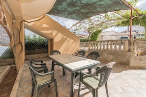 Un patio exterior con mesa y sillas, una pérgola y vista a la calle.