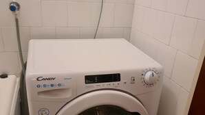 A compact, white front-loading washing machine with a digital display and control panel, situated in a small, tiled bathroom. - Apartment Cosy Terrace (Sibenik)